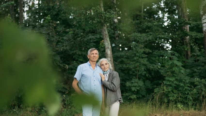 A senior couple standing together affectionately in a lush forest setting.