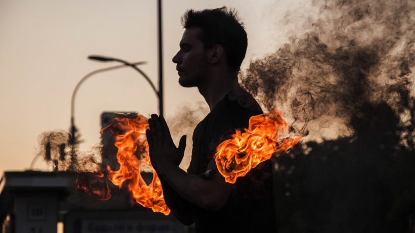 Silhouette of a man with fiery arms against the dusk sky, creating a dramatic visual.
